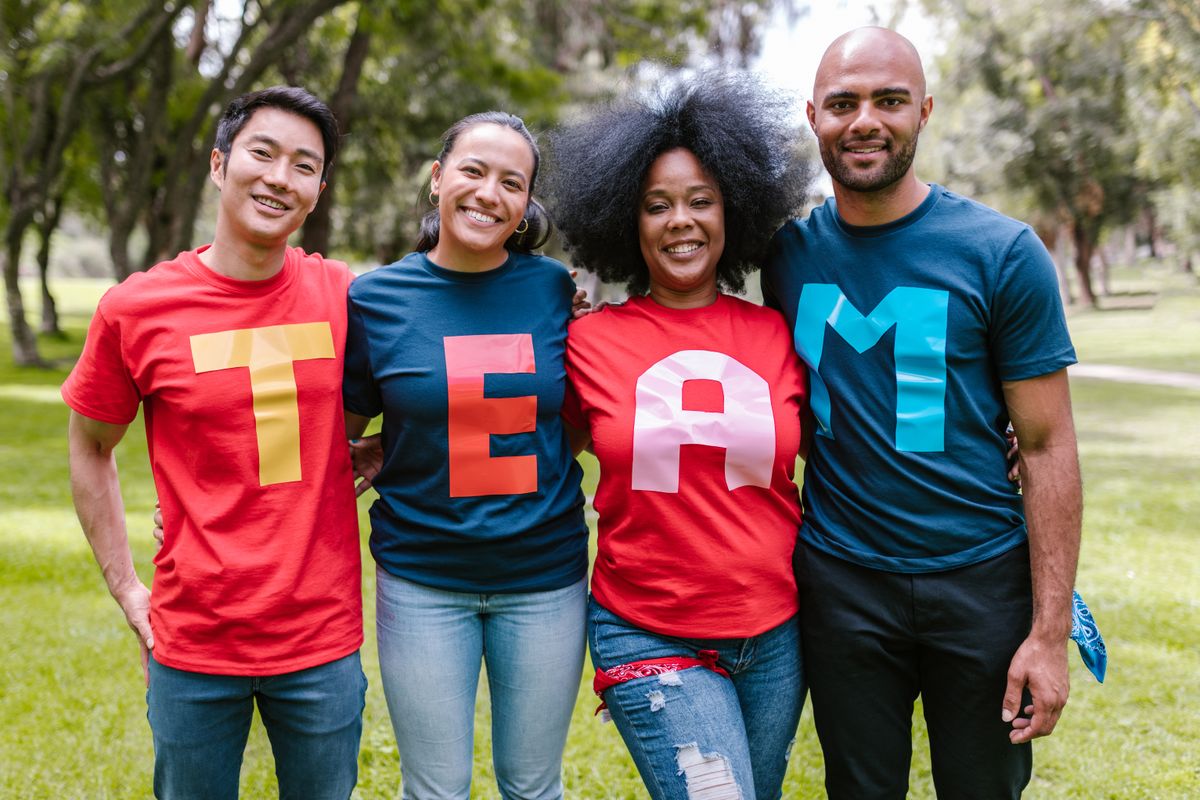 Vier mensen in felgekleurde shirts die samen het woord TEAM vormen