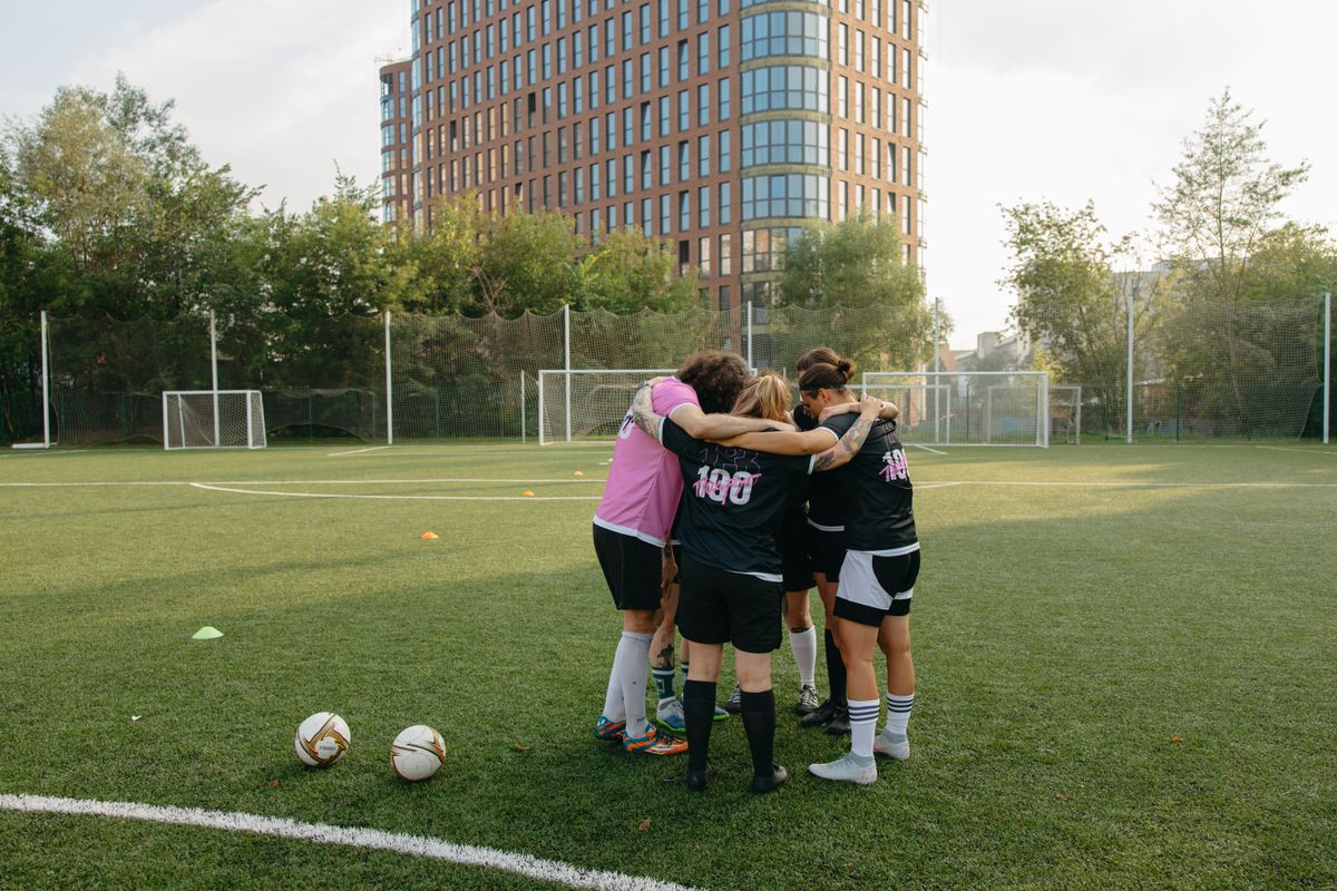 Voetbalsters in een kring op het veld, met rugnummers op de shirts
