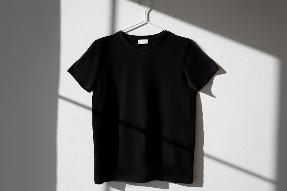 Zwart T-shirt aan een hanger tegen een lichte muur met slagschaduw
